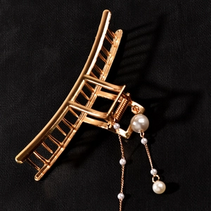 Detail of golden metal hair claw clip with elegant dangling pearl tassels on black fabric