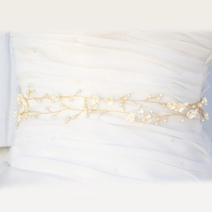 Detail of bridal belt with handmade pearl flowers on white wedding dress fabric