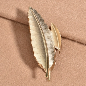 Pince à cheveux élégante en métal doré KC en forme de plume sur un fond en tissu beige