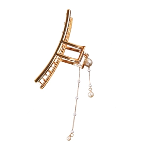 Detail of golden metal claw clip featuring elegant long pearl tassels on white background