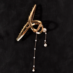 Detailed macro view of gold metal hair claw clip featuring elegant hanging pearl tassels