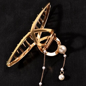 Detail of gold metal hair claw clip with hanging pearl tassels on black fabric