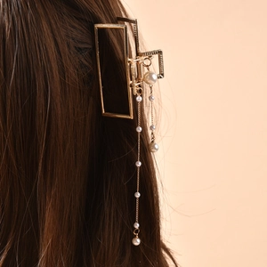 Elegant gold metal hair claw clip with long pearl tassels on wavy brown hair