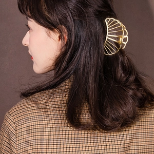 Gros plan d'une pince à cheveux en métal doré en forme d'éventail sur cheveux