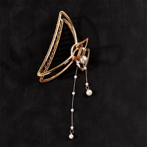 Detail of golden hollow triangle hair claw clip with white imitation pearls and long tassels