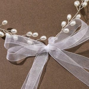 Detail of bridal hair vine with white pearls and a large organza bow on dark surface