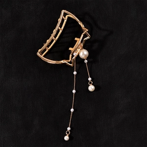 Detail of golden cat-ear hair claw clip with elegant pearl tassels on black velvet