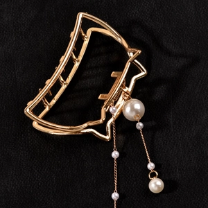 Detailed close-up of golden metal cat hair claw clip with pearl tassel and hollow design