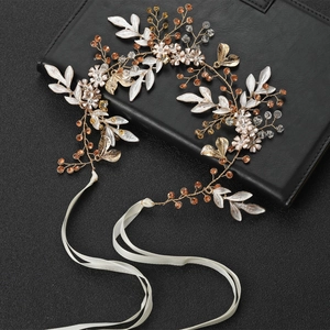 Golden bridal headband with enamel leaves, silk flowers and sparkling crystals on black surface