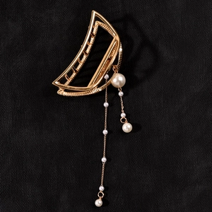 Detail of golden hollow hair claw clip with elegant dangling pearl tassels on black velvet