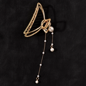 Close-up of golden metal hair claw clip with elegant pearl tassels on black background