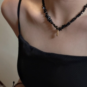 Détail d'un collier de pierres noires minimaliste avec un pendentif goutte d'eau dorée