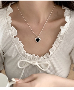 Detail of silver heart pendant necklace with black enamel inlay on a female model