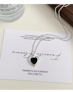 Macro shot of silver heart pendant with black enamel inlay on elegant cursive art card