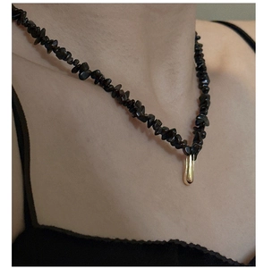 Détail macro de perles noires irrégulières et d'un pendentif goutte dorée sur le collier