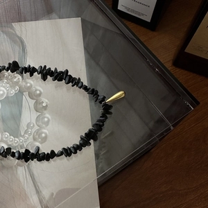 Détail des perles en pierre noire irrégulières et du pendentif goutte dorée du collier