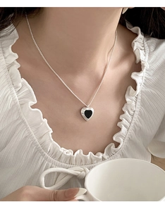 Close-up of a silver heart pendant necklace with black enamel inlay on a female model