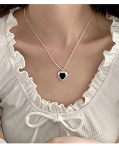 Close-up of heart pendant necklace with black glaze inlay and silver sunburst frame