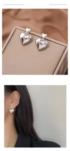 Detail of silver heart drop earrings featuring dual polished hearts on beige display