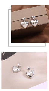 Detail of silver double heart earrings hanging on leather box and lying on beige card
