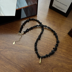 Collier minimaliste en perles noires avec pendentif goutte dorée sur fond de bois