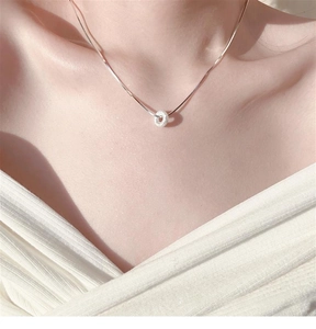 Close-up of minimalist silver donut pendant necklace with white crystals on a neck model