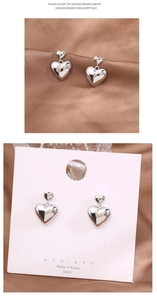 Detail of silver S925 heart earrings with shiny finish on brown silk and card