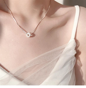 Close-up of a silver frosted donut pendant necklace worn on a woman's collarbone