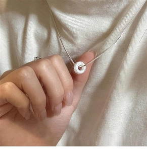 Close-up of minimalist frosted donut pendant necklace worn on a cream sweater