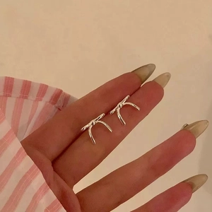 Détail d'une boucle d'oreille nœud argentée tenue entre les doigts pour la taille