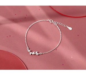 Detailed view of silver ginkgo leaf bracelet with lobster clasp on elegant pink background