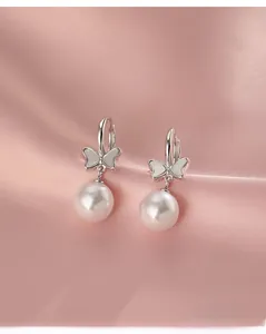 Detailed view of silver bow pearl earrings displayed on elegant pink silk fabric