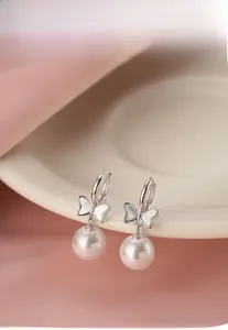 Detail showing shell bow earrings with pearls hanging on a light colored ceramic dish