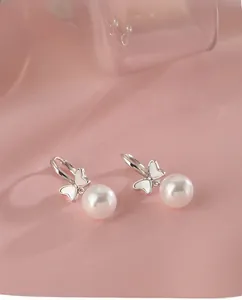 Detailed macro view of silver bowknot pearl earrings on elegant pink silk background