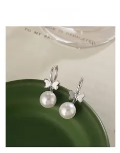 Detail of silver bow earrings with mother-of-pearl wings and white pearl drops