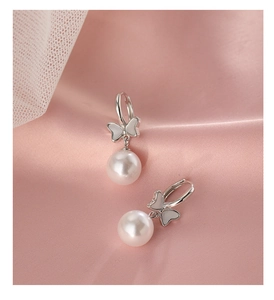 Close-up of bow-knot pearl earrings with shell inlay on soft pink satin fabric background