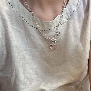 Gros plan d'un collier à grosse chaîne argentée avec pendentif cœur gravé LUCKY