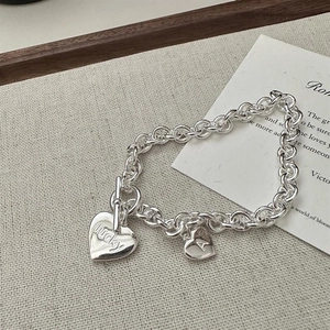 Détail du collier à fermoir OT argenté avec deux pendentifs cœurs gravés sur fond en tissu