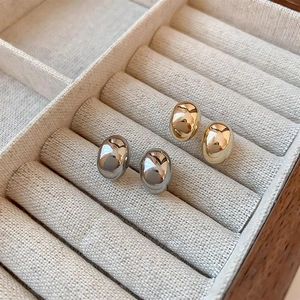 Detailed close-up of minimalist gold and silver bean stud earrings in a luxury jewelry box