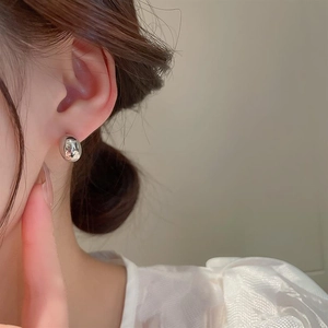 Close-up of minimalist bean-shaped silver stud earrings worn on ear with soft lighting