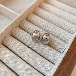 Close-up of silver-tone oval bean earrings with mirror polish on cream velvet