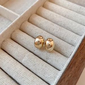 Macro detail of gold bean earrings with a polished mirror finish on beige jewelry display