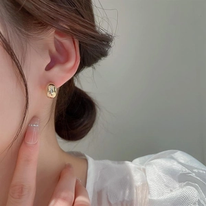 Close-up of elegant gold oval stud earrings with high-polish mirror finish on model