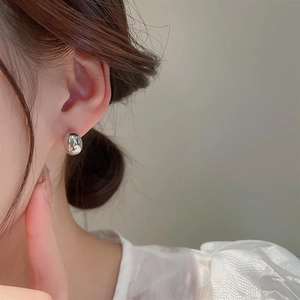 Close-up of polished silver bean-shaped earrings worn by a model in a minimalist style