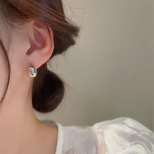 Close-up of polished silver bean stud earrings worn by a model in a minimalist style