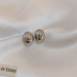 Macro shot of silver bean stud earrings on white silk fabric showing polished texture
