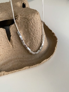 Macro shot of minimalist S925 silver necklace with square cube beads on paper holder