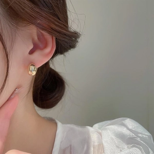 Close-up of minimalist polished gold bean stud earrings showing smooth mirror reflection