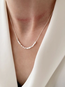 Detail of S925 sterling silver necklace with minimalist metal cube pendant on woman neck
