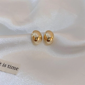 Macro detail of glossy golden bean-shaped metal stud earrings on white silk